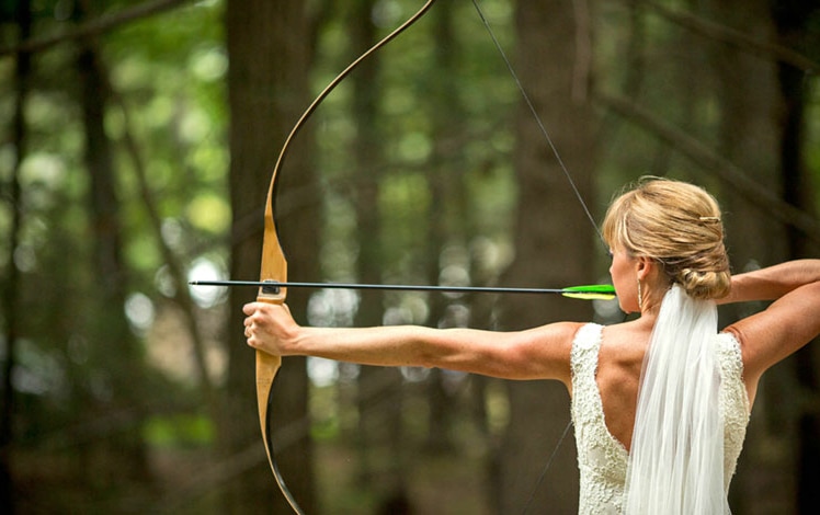 camp oneka weddings & gatherings bride in the woods aiming bow and arrow